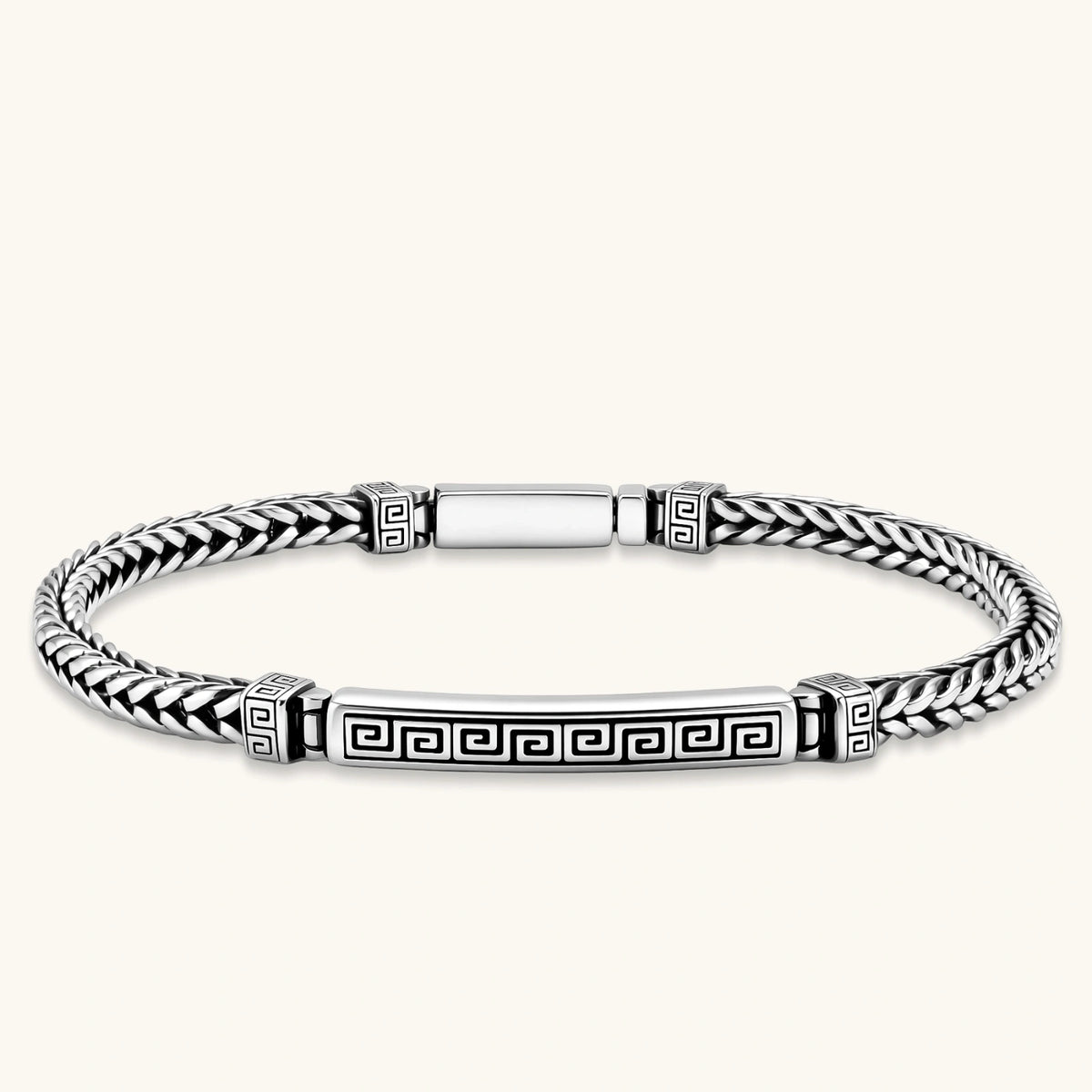 Antique silver plated chain bracelet with a Greek key engraved ID bar and patterned spacer beads on a cream background.